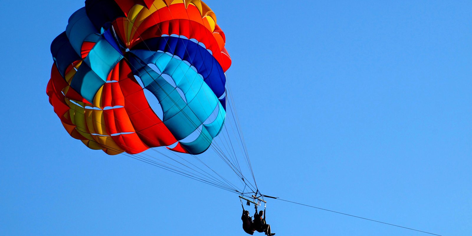 Two people under a parachute towed by a boat
