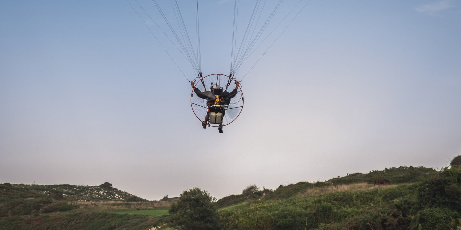 Paramotor Pilot Flying Over Green hillcountry